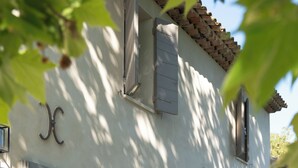 A building with arched windows and doors, a tiled roof, and a sign with a capital 'J'. - Exceptional villa with swimming pool - Direct access on foot to Château de la Gaude (Aix-en-Provence)
