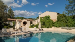 A clear swimming pool with lounge chairs and umbrellas, surrounded by greenery and a building with a tiled roof. - Exceptional villa with swimming pool - Direct access on foot to Château de la Gaude (Aix-en-Provence)
