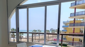 A room with a large window overlooking a beach and a multi-story building. There is a table with two chairs and a blue tray. - Front line, sea view, wifi, parking (Unknown)