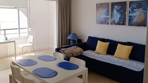 A room with a dining table, chairs, a sofa with cushions, a lamp, and artwork on the wall. - Front line, sea view, wifi, parking (Unknown)