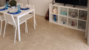 A dining area with a white table set for four, a television on a white stand, and a wall-mounted shelf with various items. - Front line, sea view, wifi, parking (Unknown)