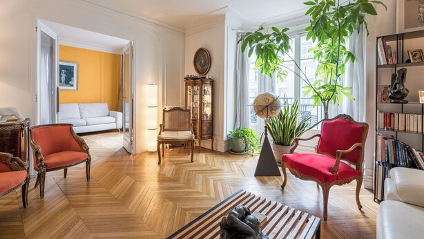 Un salon spacieux avec un parquet en point de Hongrie, un canapé blanc, un fauteuil rouge, une chaise en bois et une bibliothèque.