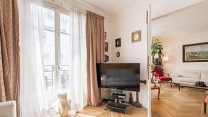 Un salon doté d’un grand téléviseur à écran plat, d’un canapé, d’un fauteuil rouge et d’un parquet en bois.
