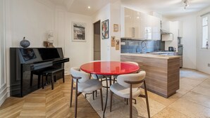 Une cuisine moderne avec des meubles blancs, un îlot central et un coin repas comprenant une table rouge et quatre chaises.