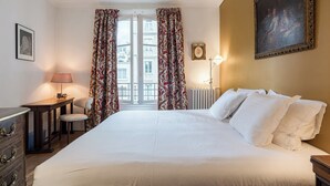 Une chambre d’hôtel avec un grand lit, un bureau avec une lampe, une chaise et une vue sur les bâtiments par la fenêtre.