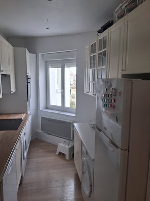 Eine kompakte Küche mit integriertem Waschmaschine, einem Fenster und einem Kühlschrank.