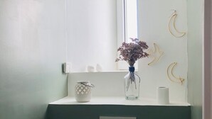 Kylpyhuoneessa on valkoinen pesuallas, peili ja maljakko, jossa on kuivattuja kukkia. Seinällä on puolikuun muotoisia koristeita.
