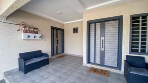 A covered outdoor area with a sofa, a bench, a door with a metal gate, and a wall-mounted electrical panel. - Villa Fafa — Comfort in style (Ho)
