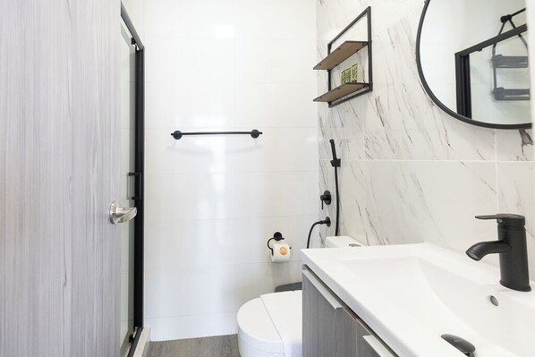 A modern bathroom with a white toilet, a sink with a black faucet, and a shower area.