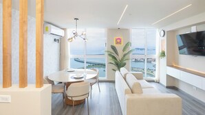 A modern living room with a large window, a dining area, and a flat-screen TV mounted on the wall.