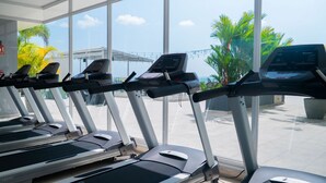 A row of treadmills in a gym with large windows and a view of palm trees.