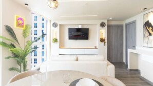 A modern living room with a TV, sofa, dining table, and plants.
