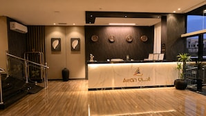 Een hotel receptie met een marmeren balie, klokken, een potplant en een trap.