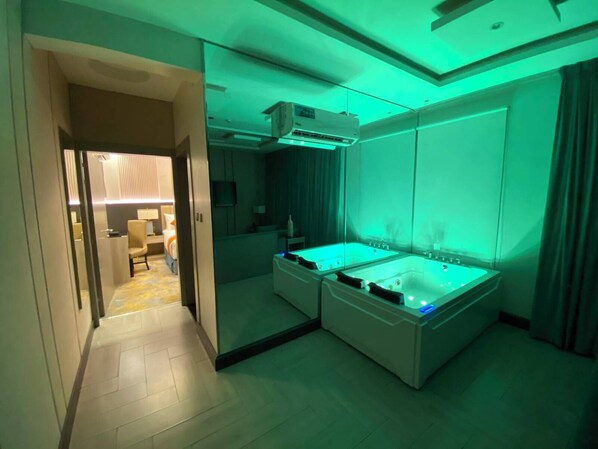 A hotel room with a large bathtub, a separate shower area, and a glass door leading to a hallway.