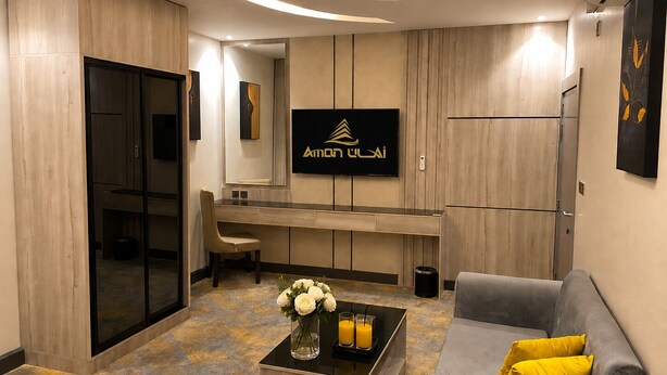 Een moderne hotelkamer met een bureau, een bank, een bijzettafeltje met bloemen en een aan de muur bevestigde televisie.