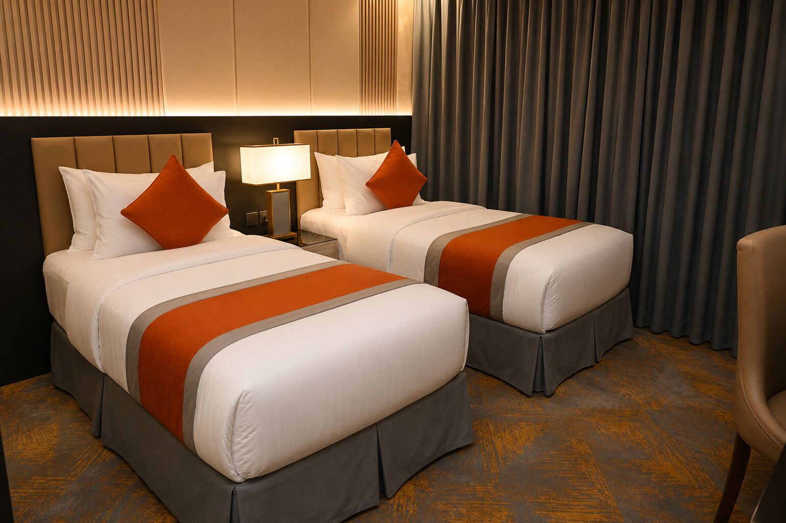 Habitación de hotel con dos camas, una mesita de noche con lámpara y vistas al exterior a través de cortinas.