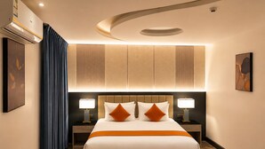 Een hotelkamer met een groot bed, twee nachtkastjes met lampen, een plafondlamp en een wandairconditioner.
