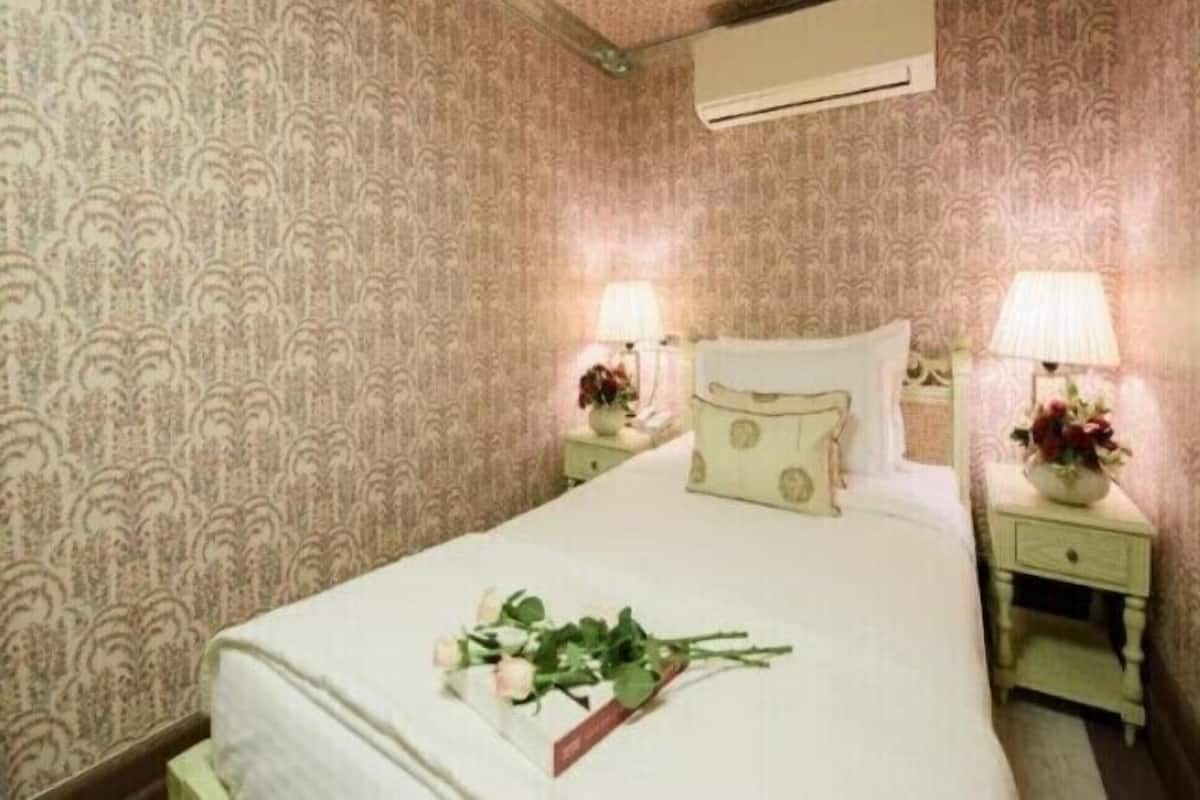 A neatly made bed with a floral arrangement, two bedside lamps, and a patterned wallpaper.