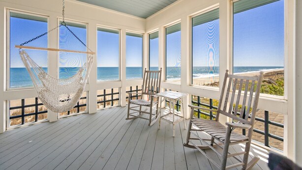 Een overdekt terras met een hangmat, stoelen en een tafel met uitzicht op het strand.