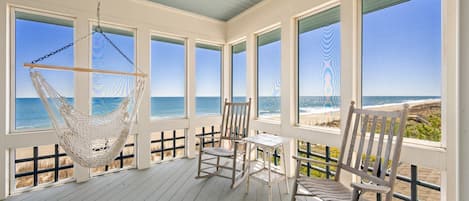 Terraza techada con una hamaca, sillas y una mesa con vista a la playa.