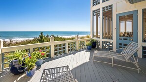 Een balkon met uitzicht op de oceaan, twee witte stoelen en potplanten.