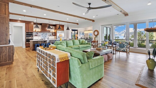 A spacious living area with a green sofa, wooden flooring, and a kitchen in the background. - Beautiful 9-Bedroom Coastal Retreat Second-Row, Ocean Views with Private Pool! (Georgetown)