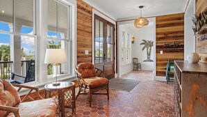 A spacious room with a wooden floor, large windows, and a view of the outdoors. There are wicker chairs and a small table. - Beautiful 9-Bedroom Coastal Retreat Second-Row, Ocean Views with Private Pool! (Georgetown)