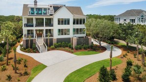A two-story house with a balcony, a covered patio, and a landscaped driveway. - Beautiful 9-Bedroom Coastal Retreat Second-Row, Ocean Views with Private Pool! (Georgetown)