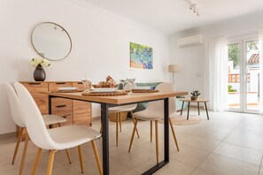 A dining area with a wooden table, white chairs, a vase with flowers, and a painting on the wall.