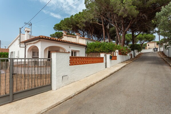 Una calle residencial con casas, un acceso con portón y árboles.