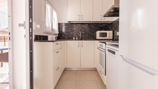 A compact kitchen with white cabinets, a microwave, an oven, and a sink.