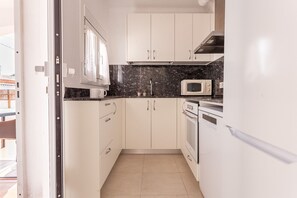 Une cuisine de taille réduite avec des meubles blancs, un four à micro-ondes, un four traditionnel et un évier.