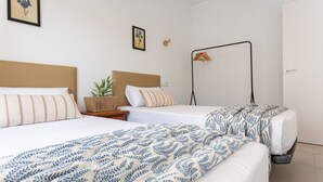 Une chambre d’hôtel avec deux lits, une table de chevet ornée d’une plante, une lampe fixée au mur et une porte.