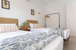 Une chambre d’hôtel avec deux lits, une table de chevet ornée d’une plante, une lampe fixée au mur et une porte.
