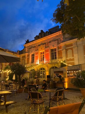 An outdoor cafe area with tables and chairs, a building with classical architecture, and string lights. - A family-friendly stopover in the heart of Fontainebleau (Fontainebleau)