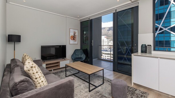 Un salon moderne avec un canapé, une table basse, un téléviseur et un balcon offrant une vue sur la ville.
