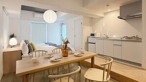 A modern kitchen with white cabinets, a microwave, and a stove. There is a dining area with a wooden table and chairs. - Arts Dobashi 3N (Hiroshima)