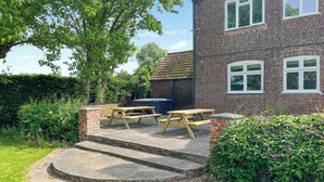 A patio with a picnic table and a barbecue grill in front of a brick house.