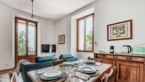 Un comedor con una mesa preparada para cuatro personas, un sofá, un televisor y una zona de cocina con cafetera y hervidor.