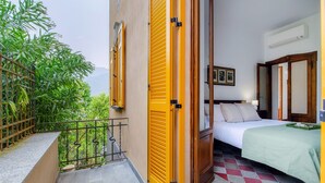 Una habitación de hotel con balcón, una cama con colcha verde y vista a zonas verdes.