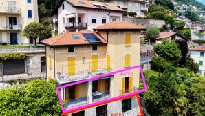Un edificio de varios pisos con balcones, fachada de piedra y vistas a una comunidad en la ladera.