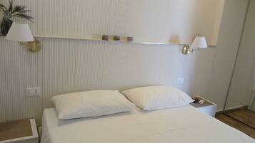 A hotel room with a large bed, two bedside lamps, a small table, and a wall-mounted shelf with decorative items.