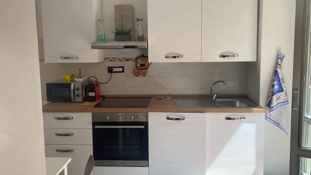Una cocina moderna con armarios blancos, horno empotrado, microondas y un lavamanos.