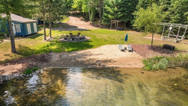 A pond surrounded by a grassy area with a swing set and a small deck. - Turtle Lake Beach House - Get Up North Retreats (Bigfork)