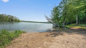 A sandy beach with a calm lake, surrounded by trees and a clear sky. - Turtle Lake Beach House - Get Up North Retreats (Bigfork)