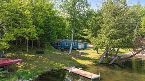 A house by a lake with a dock extending into the water. - Turtle Lake Beach House - Get Up North Retreats (Bigfork)