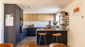 A modern kitchen with dark cabinets, a wooden island with stools, and a fruit bowl on the table. - Stylish Family Home with Garden (Bristol)