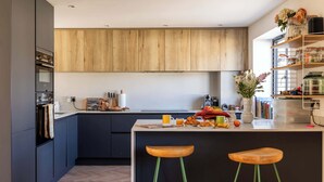 A modern kitchen with dark cabinets, wooden countertops, and a central island with stools. - Stylish Family Home with Garden (Bristol)