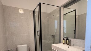 Un baño moderno con cabina de ducha de vidrio, inodoro y tocador con espejo.