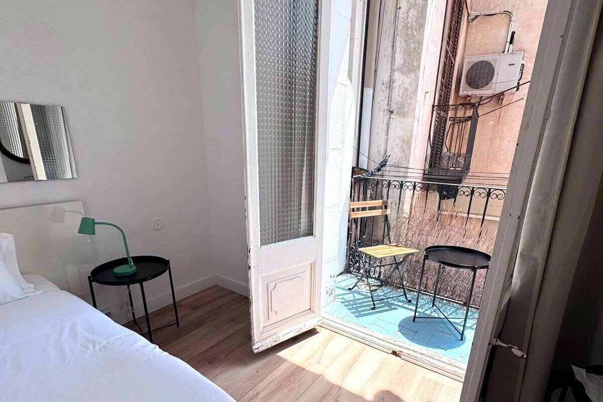 A bedroom with a bed, a small table with a lamp, and a balcony with a table and chairs.